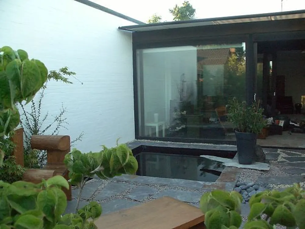 Minimalistische Terrasse mit weißer Ziegelwand, versenktem Wasserbecken und Grünpflanzen