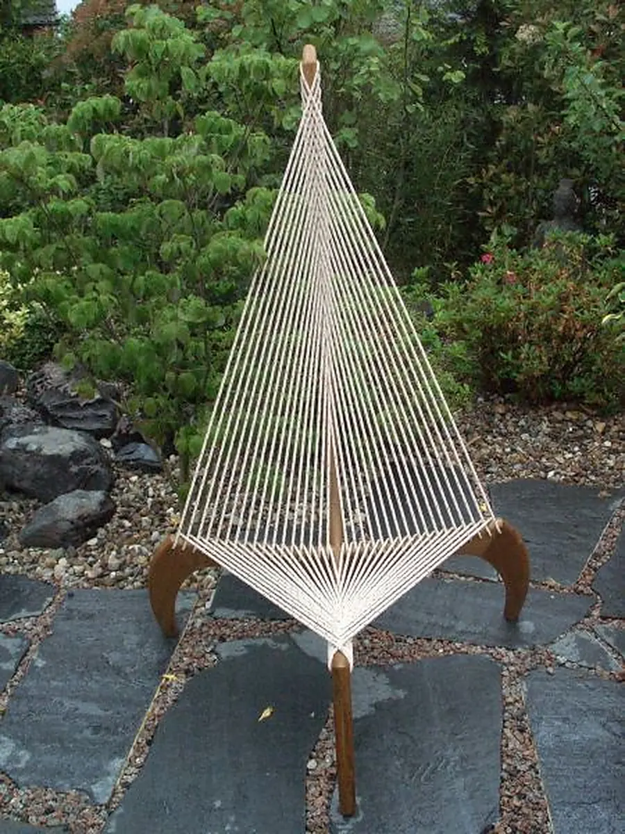 Minimalistischer Stuhl mit Holzgestell und weißer Kordelbespannung im grünen Garten