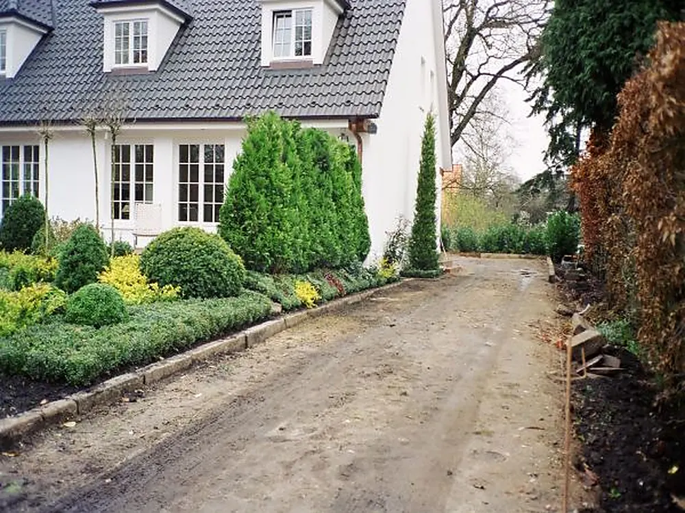 Weißes Wohnhaus mit gepflegtem Garten, Buchsbäumen und Kiesweg